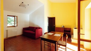 A room with a red sofa, a wooden dining table, and a tiled floor. - Cottages surrounded by nature and relaxation in the Dauni Mountains (ROSETO VALFORTORE)