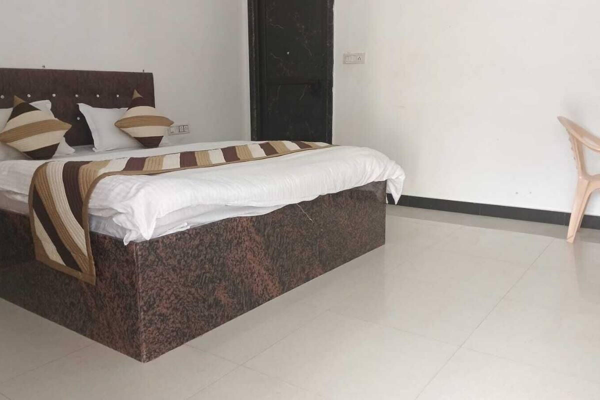 Ein ordentlich bezogenes Bett mit einem gemusterten Bettdeckenüberwurf und Kissen, ein Holz-Kopfteil und eine schlichte Wand mit einer Tür.