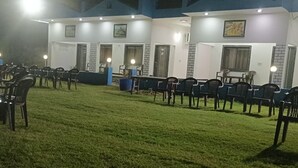 Un espace extérieur aménagé avec des chaises et des tables, un bâtiment doté de nombreuses portes et fenêtres, et un environnement bien éclairé.