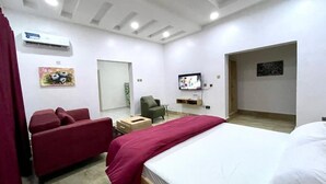 A hotel room with a bed, a red sofa, a small table, and a TV. - Tupon Luxury Apartment (Abuja)
