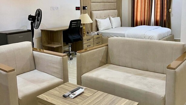 Een moderne hotelkamer met een bank, een klein houten tafeltje, een lamp, een ventilator en een bed.