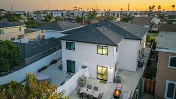 A modern two-story house with a patio, a covered outdoor seating area, and a view of neighboring houses.