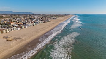 An aerial view of a coastal city with a wide beach, dense residential area, and clear blue sky.