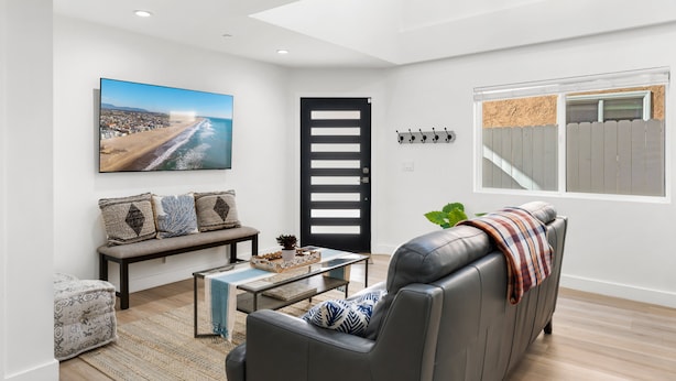 Ein modernes Wohnzimmer mit einem großen Fenster, einer schwarzen Tür, einer Bank, einem Sofa und einem Couchtisch.