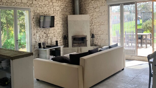 Amplia sala de estar con pared de piedra, chimenea, sofá y puerta corrediza de vidrio que da a un patio exterior.