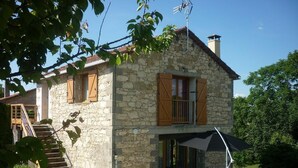 Una casa de piedra con contraventanas de madera, un porche cubierto y una escalera que lleva a la entrada.