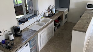 Una cocina con un lavamanos, estufa y microondas. Hay una ventana sobre el lavamanos y un reloj en la pared.
