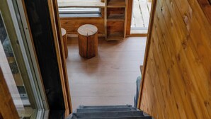 Un escalier en bois mène à une mezzanine dotée d’une fenêtre donnant sur un espace verdoyant.