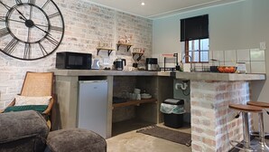 Een compacte keuken met een grote wandklok, een magnetron, een koffiezetapparaat en een koelkast.