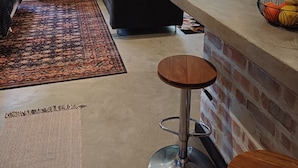 Een moderne woonkamer met een bank, een houten dressoir, een eethoek met een barkruk en een accentmuur van baksteen.