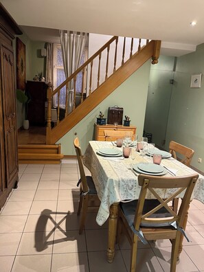 A dining area with a wooden staircase, a table set for four, and a view of the living room. - Casa Brugensis Holiday Home in Historic center of Bruges (Brugge)