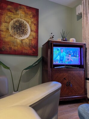 A living room with a television on a wooden cabinet, a large abstract painting on the wall, and a potted plant. - Casa Brugensis Holiday Home in Historic center of Bruges (Brugge)