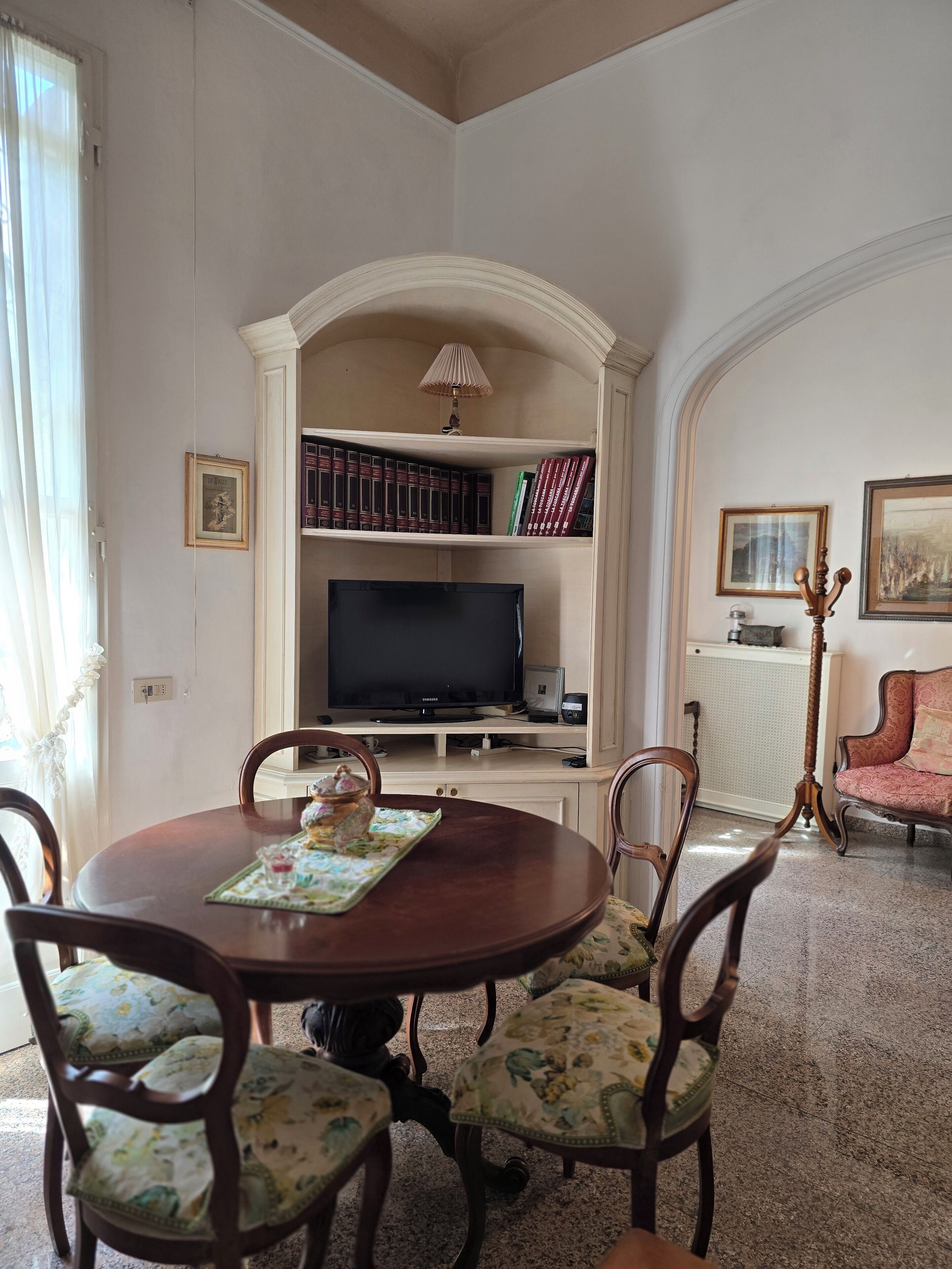 A dining area with a round table, floral chairs, a television, and bookshelves.