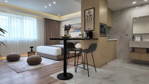 Ein modernes Hotelzimmer mit Bett, Esstisch mit Stühlen, Küchenzeile und Bad.