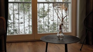 Une pièce avec une grande fenêtre, une table ronde ornée d’un vase et deux chaises.