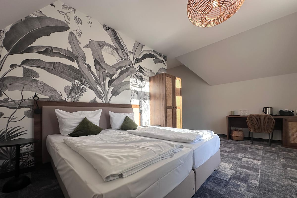 A neatly made bed with pillows, a desk with a chair, a woven light fixture, and a large plant wall.