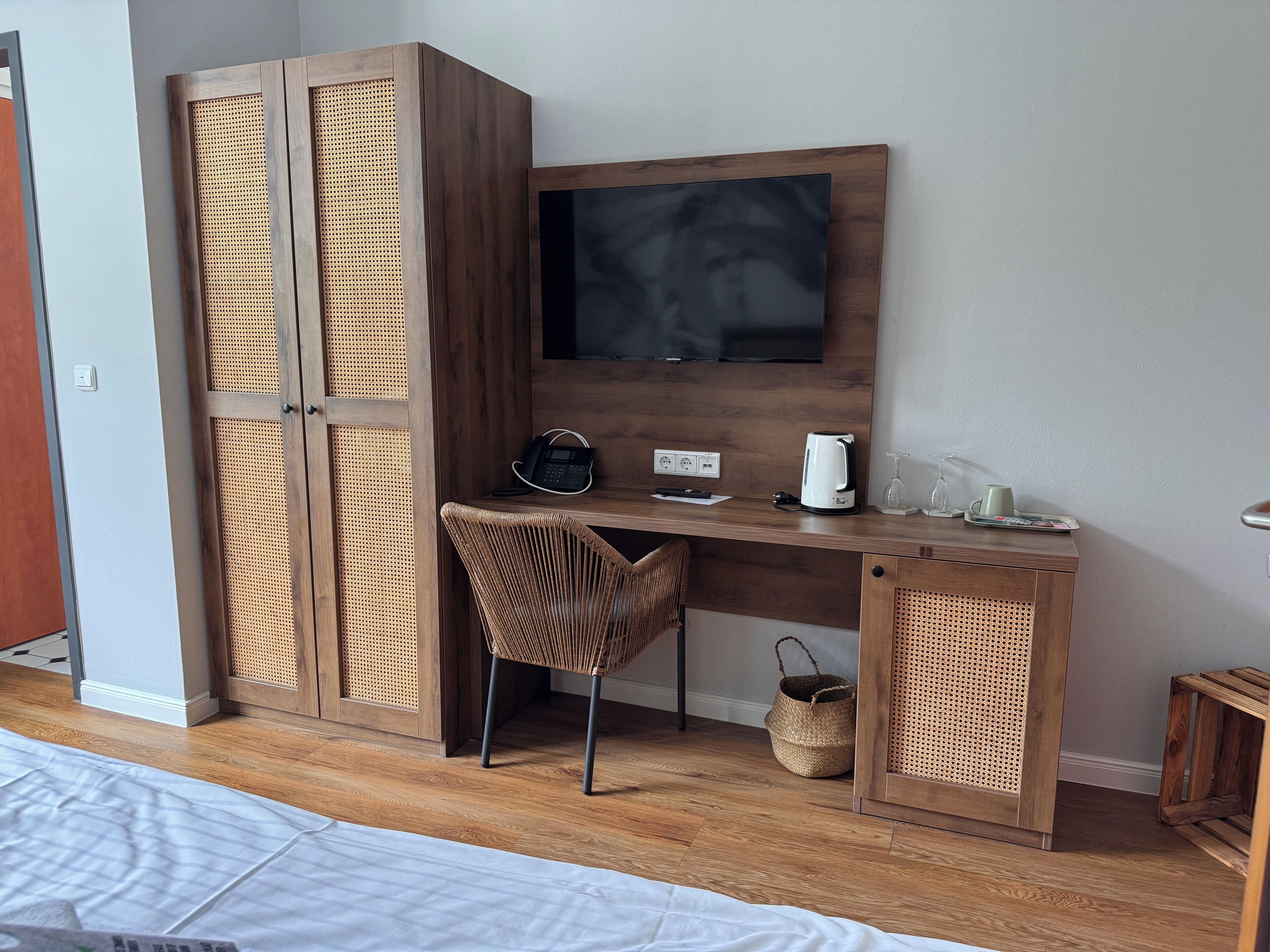 Une chambre d’hôtel équipée d’un bureau en bois, d’une chaise, d’une télévision, d’un téléphone, d’une bouilloire et d’un panier.