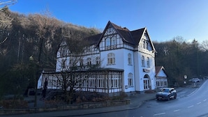 Un grand bâtiment blanc, doté d’un toit en pente et de nombreuses fenêtres, situé au bord d’une route où circulent des voitures.