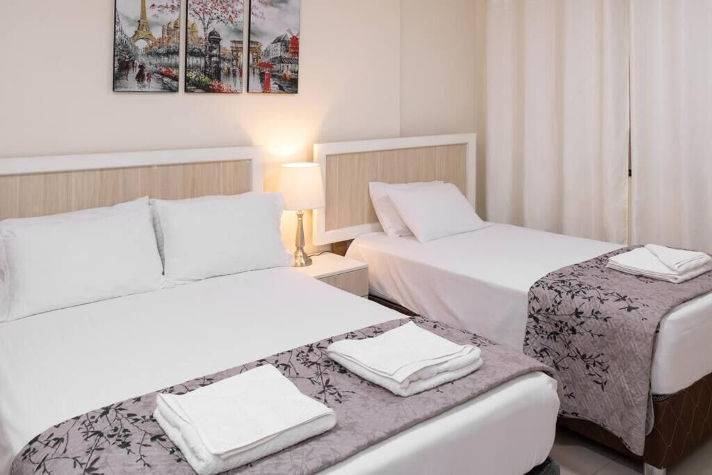 A hotel room with two beds, a nightstand, a lamp, and artwork on the wall.