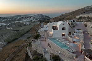 A white building with a pool and outdoor seating, surrounded by stone walls and a view of a hillside village. - Villa - Sleeps 5 - Private Heated Pool-parking (Pyrgos)