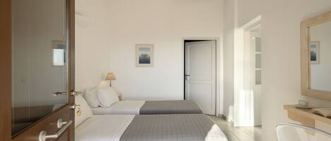 A hotel room with two beds, a wooden wardrobe, a mirror, a bedside table with a lamp, and a view of the hallway.