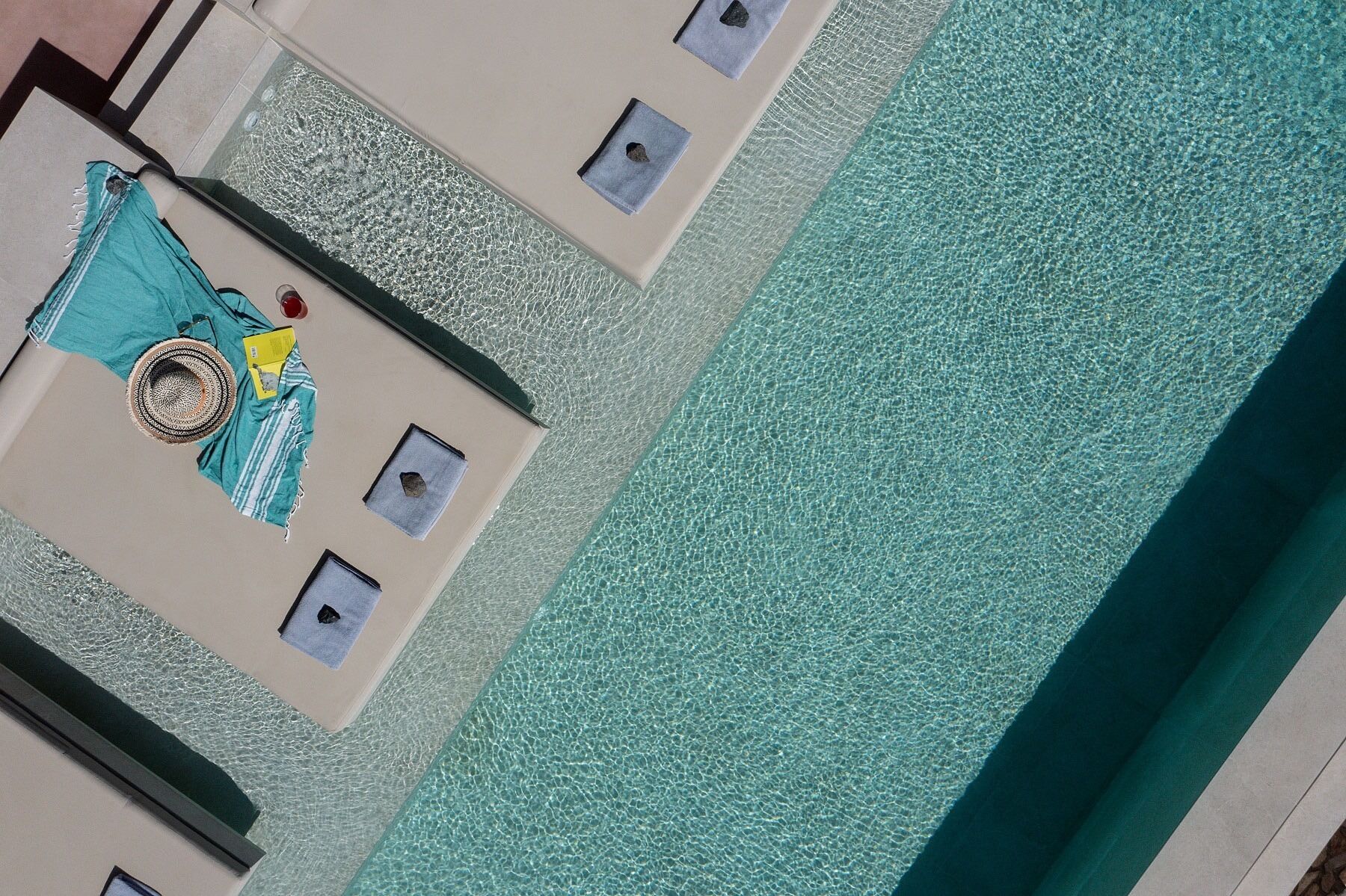 A pool with clear water, a towel, and a hat on the edge.