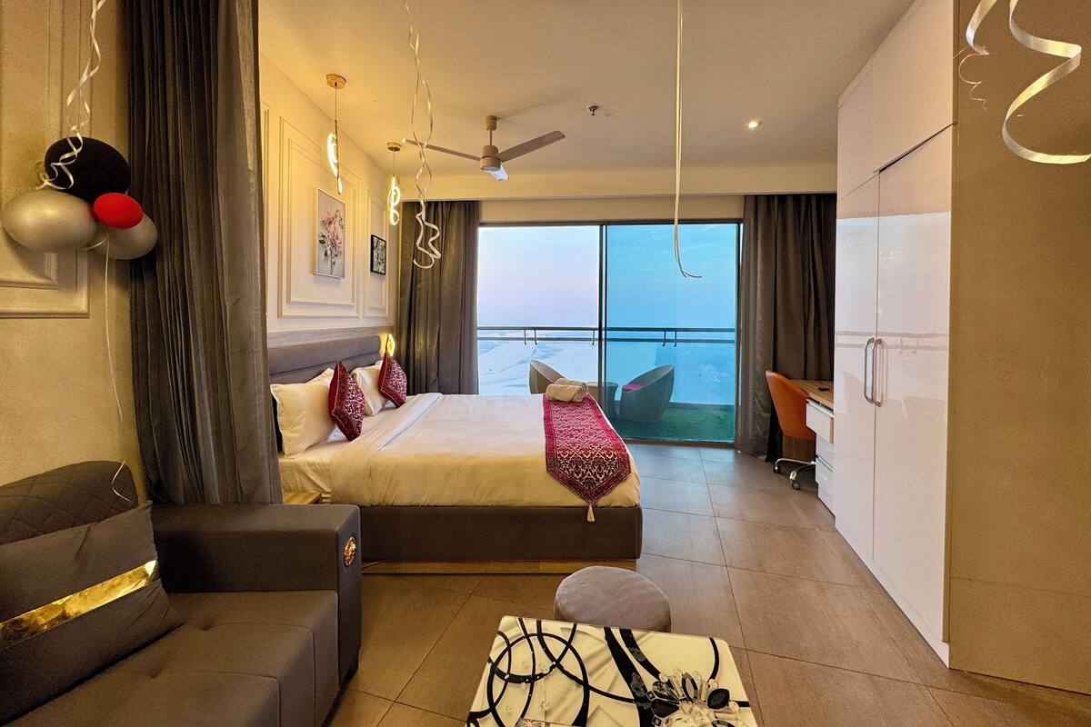 A hotel room with a bed, a sofa, a desk, and a view of the sea.