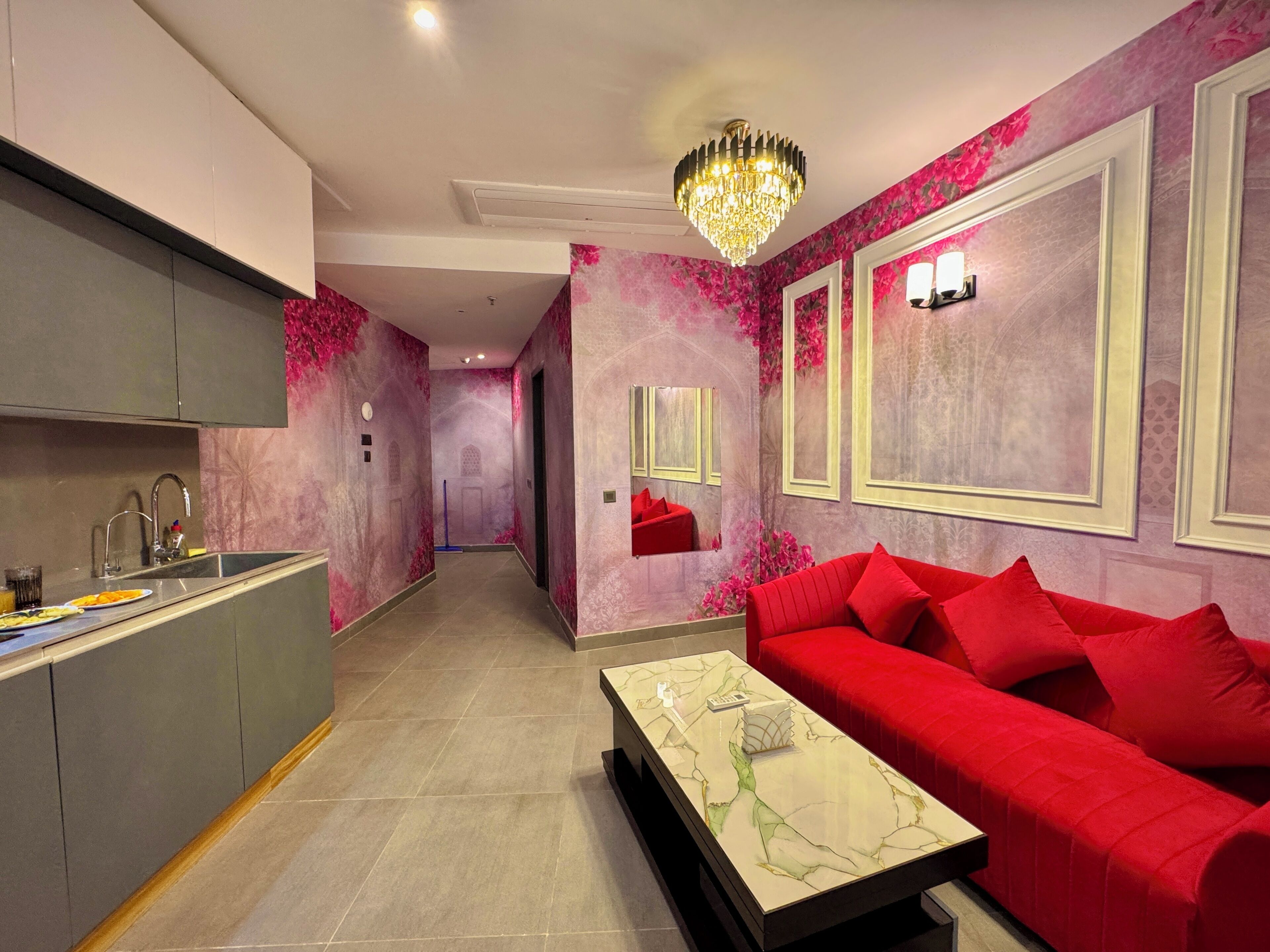 A modern kitchen with a built-in sink and a dining area with a red sofa and a marble coffee table.