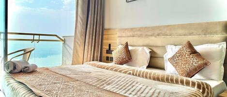 A hotel room with a large bed, a view of the sky, and two framed artworks on the wall.