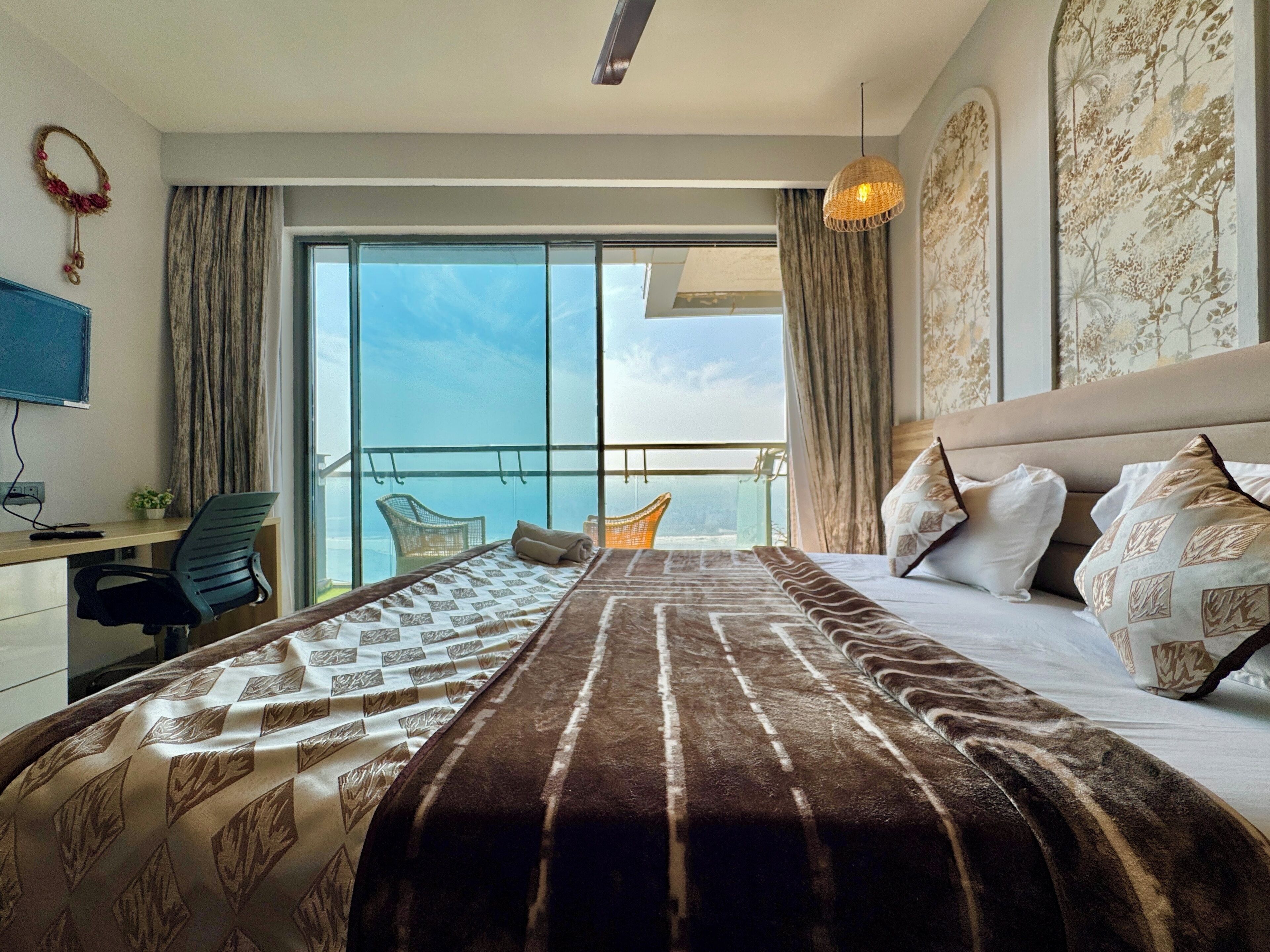 A hotel room with a large bed, a desk, a chair, and a balcony with a view.
