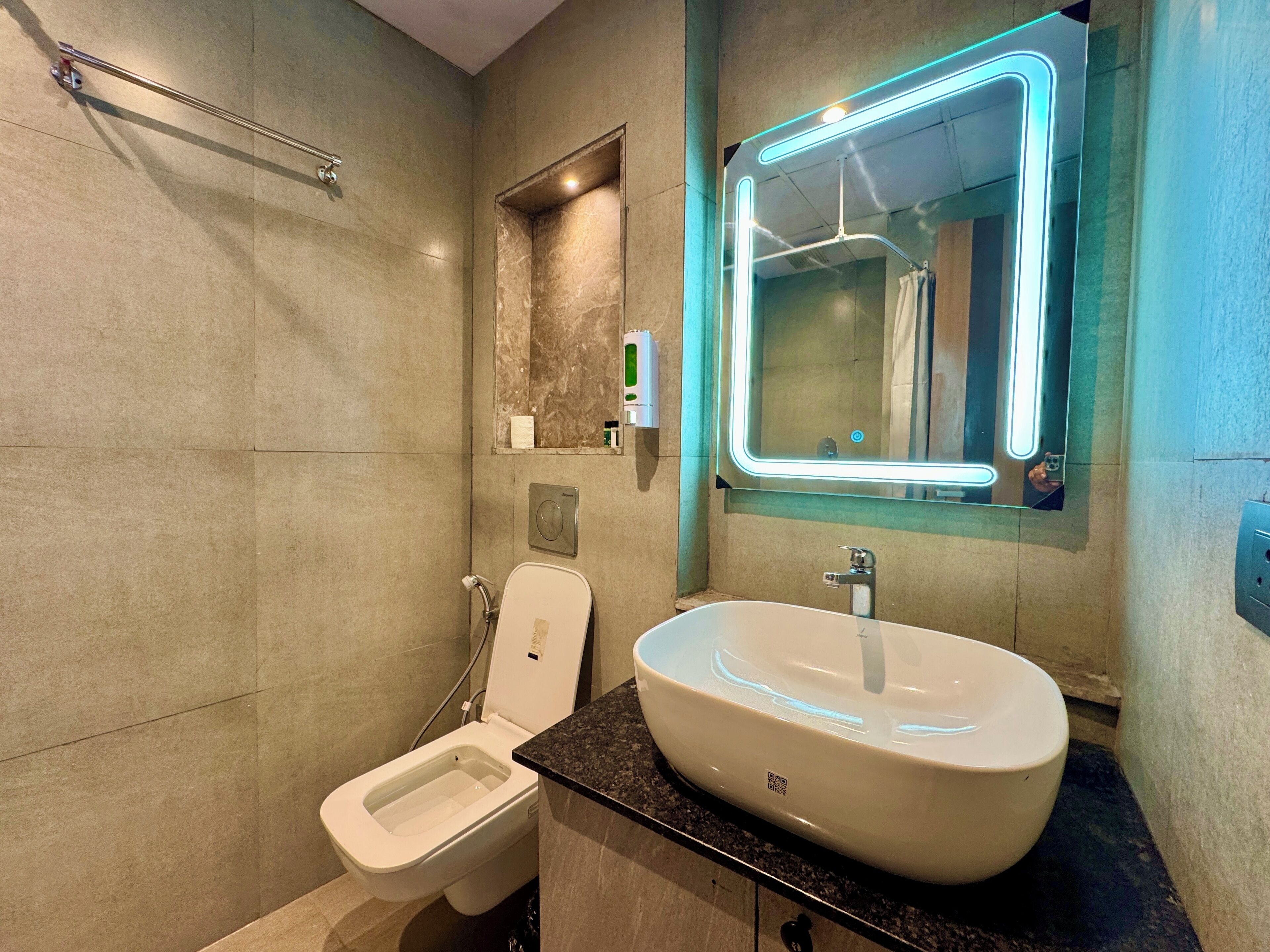 Ein modernes Badezimmer mit Toilette, großem Waschbecken und einem Spiegel mit Neonbeleuchtung.