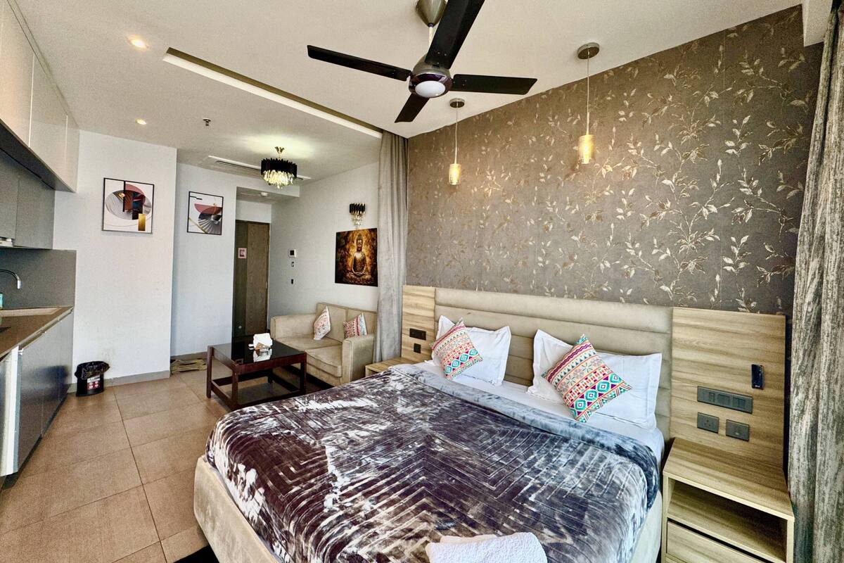 A modern hotel room with a large bed, a ceiling fan, a small desk, and a kitchenette.