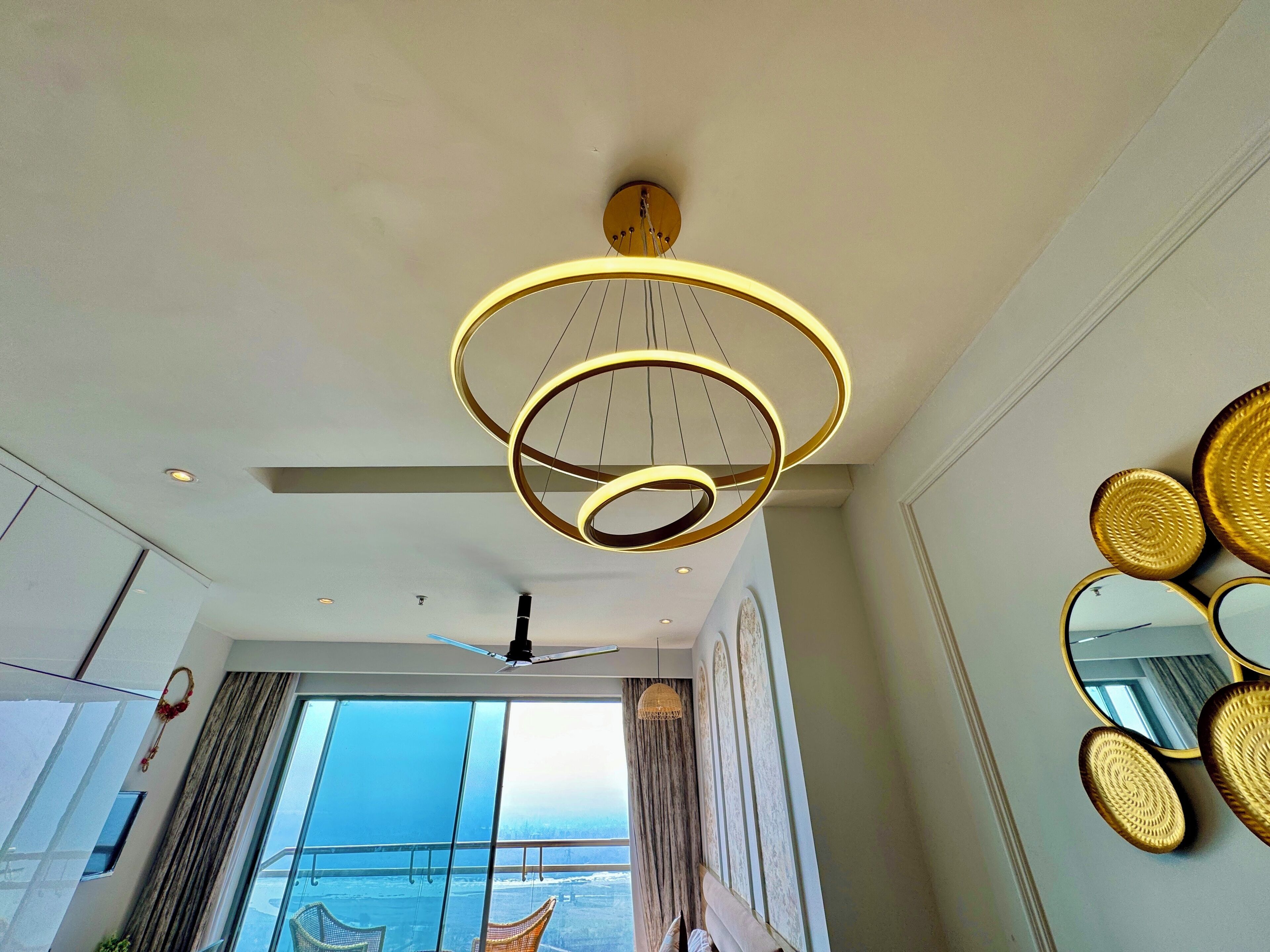 A modern interior with a large window, a ceiling fan, and a unique circular light fixture.