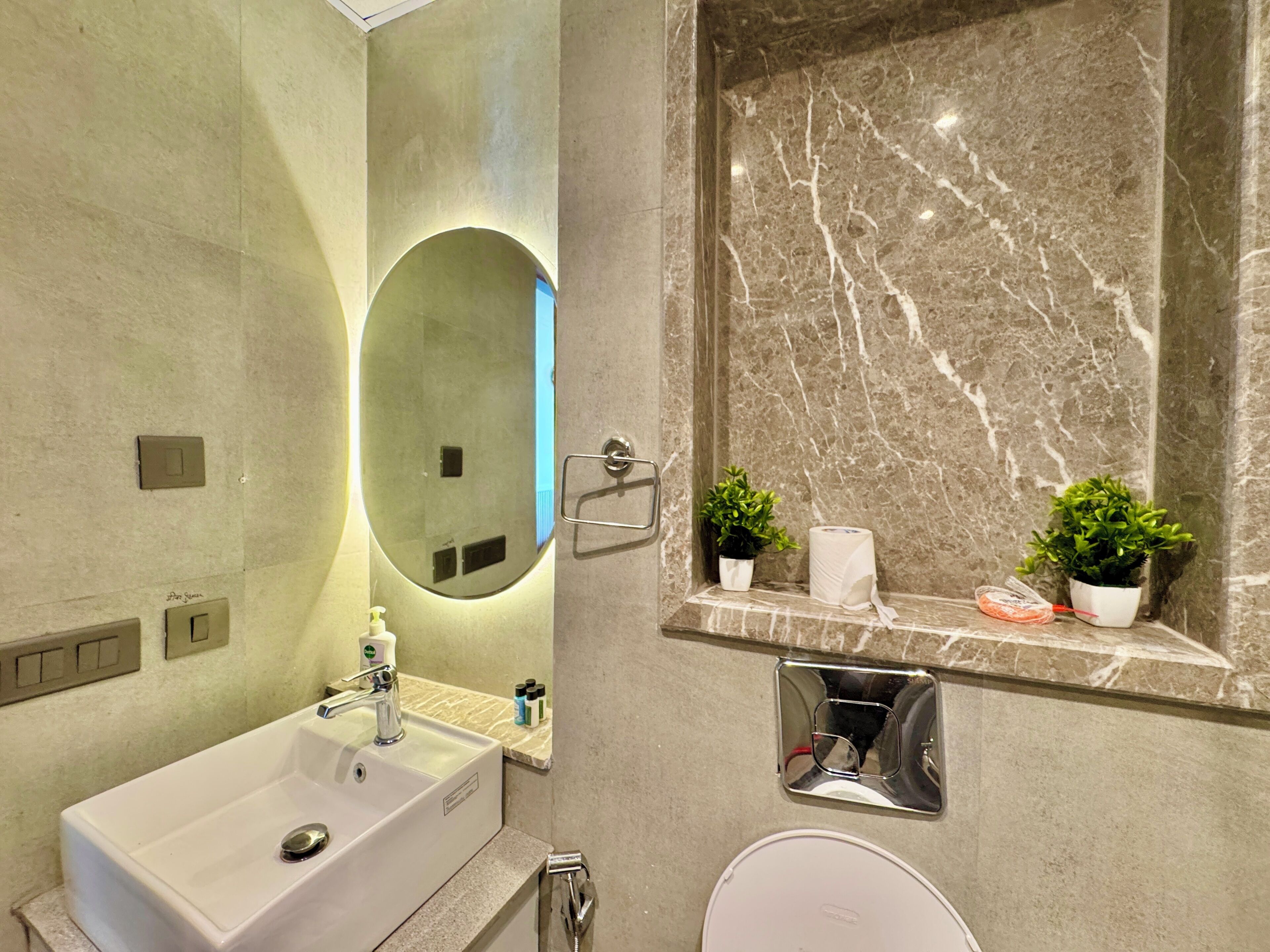 Un baño moderno con un espejo grande, un lavamanos, un inodoro y una pared de mármol.