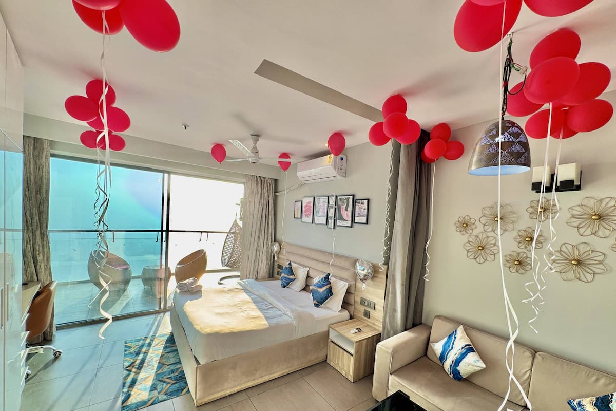 A modern bedroom with a bed, bedside tables, a sofa, and a balcony with a view.