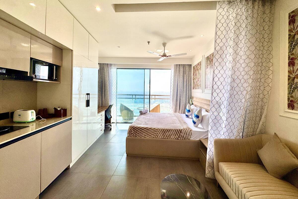 A modern hotel room with a balcony, a kitchenette, and a sofa.