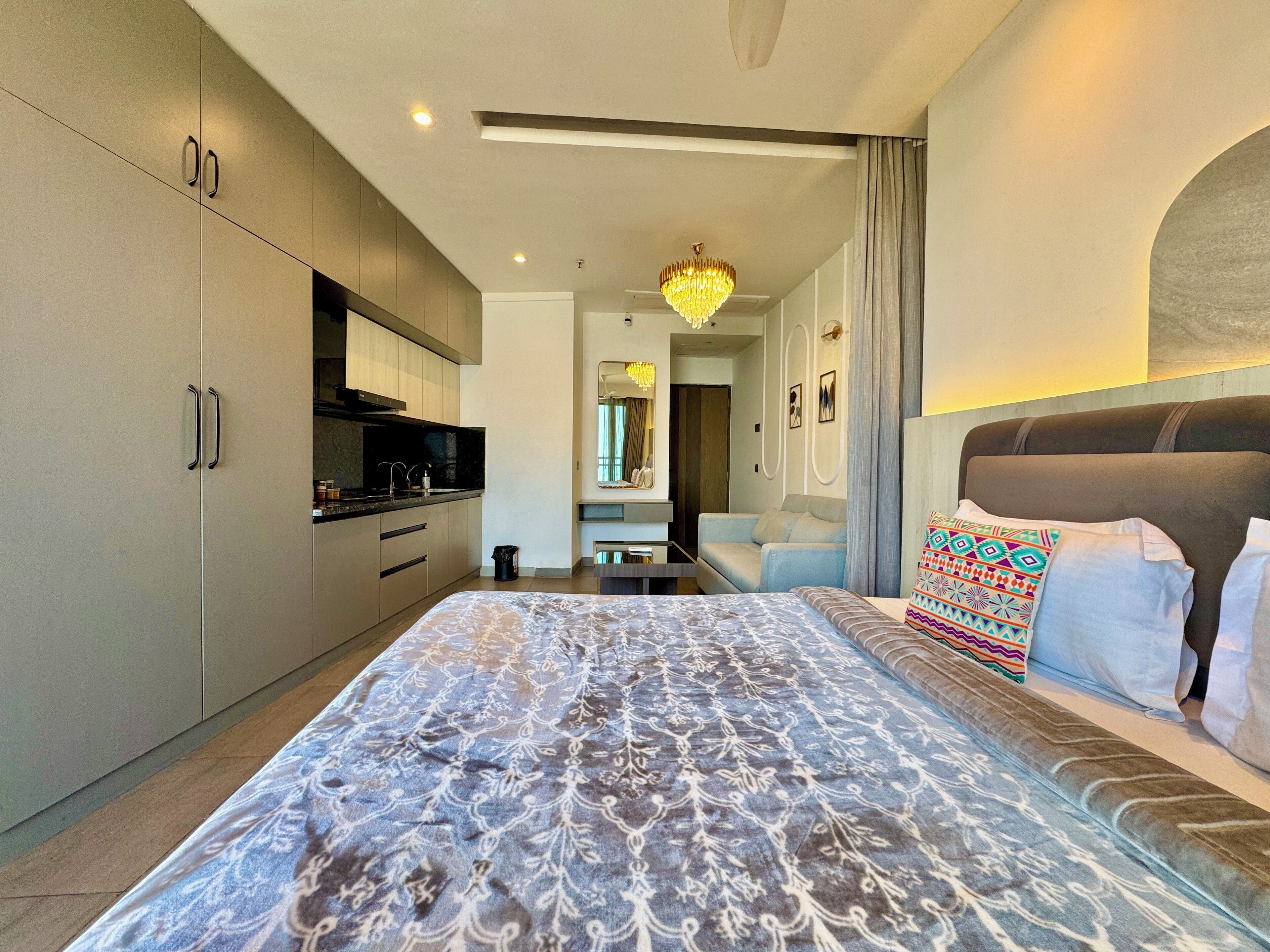 A modern hotel room with a large bed, a separate sitting area, a kitchenette, and a bathroom.