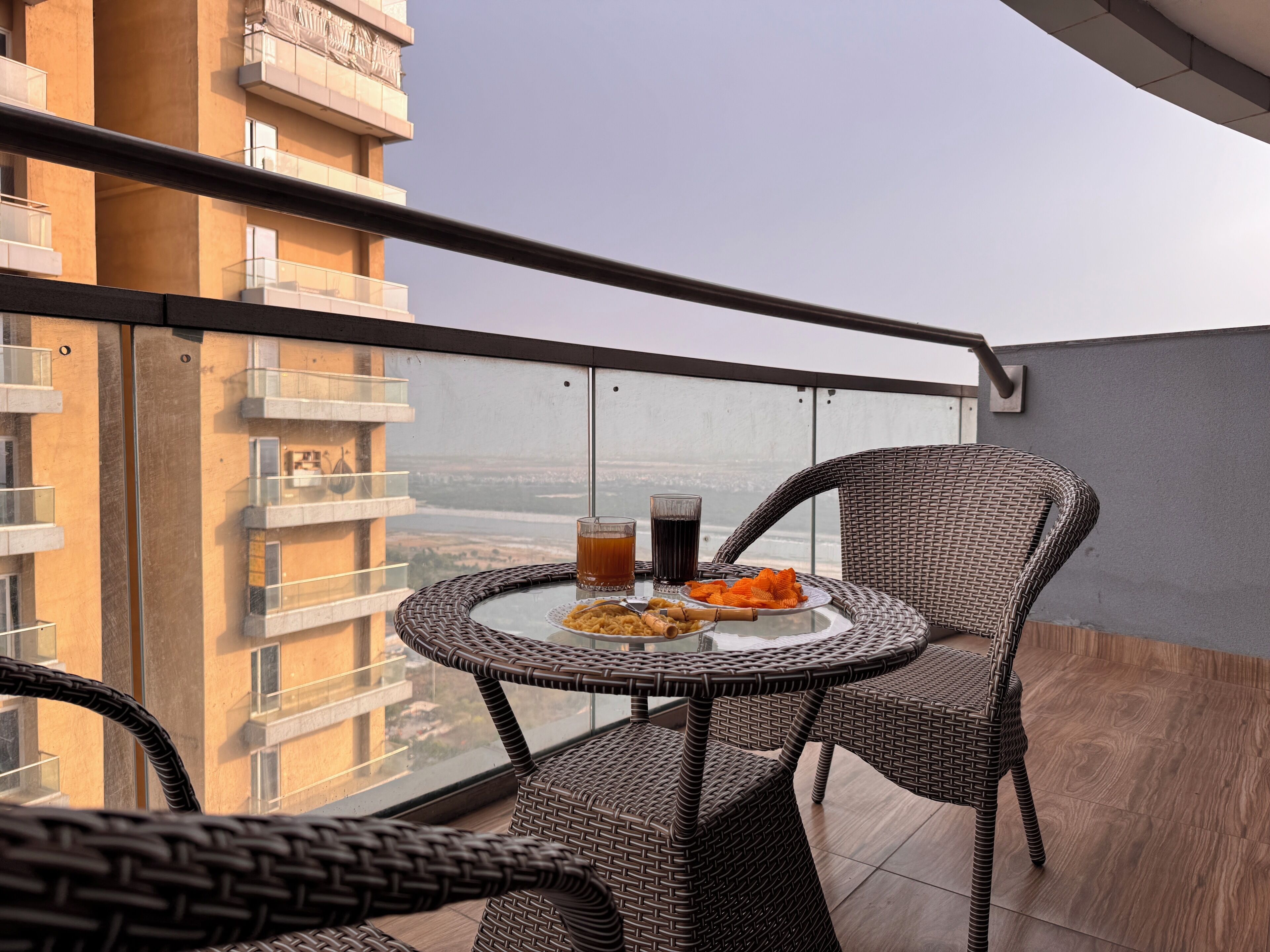 A balcony with wicker furniture, a glass table, and a view of a building.