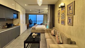 Une chambre d’hôtel moderne dotée d’une kitchenette, d’un canapé, d’une table basse et d’une grande fenêtre offrant une vue sur la ville.