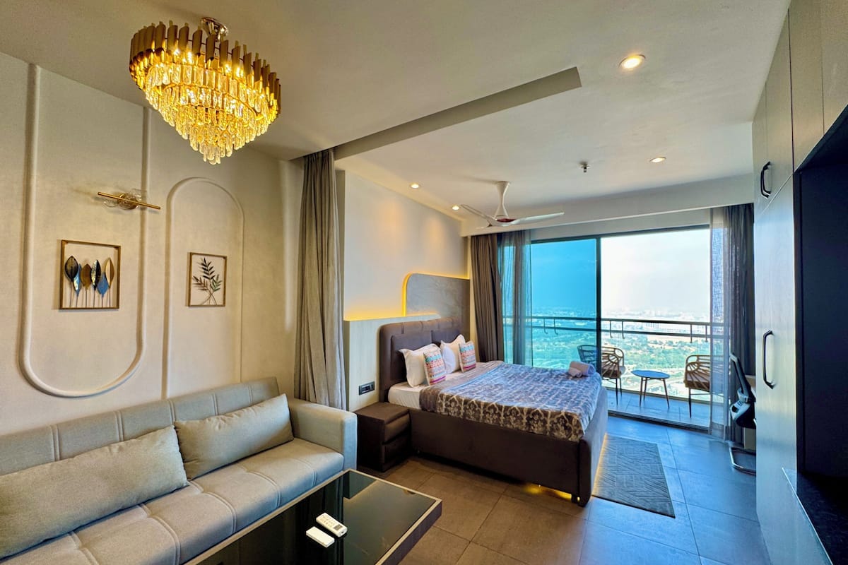 A modern hotel room with a large bed, a sofa, a glass coffee table, and a chandelier.