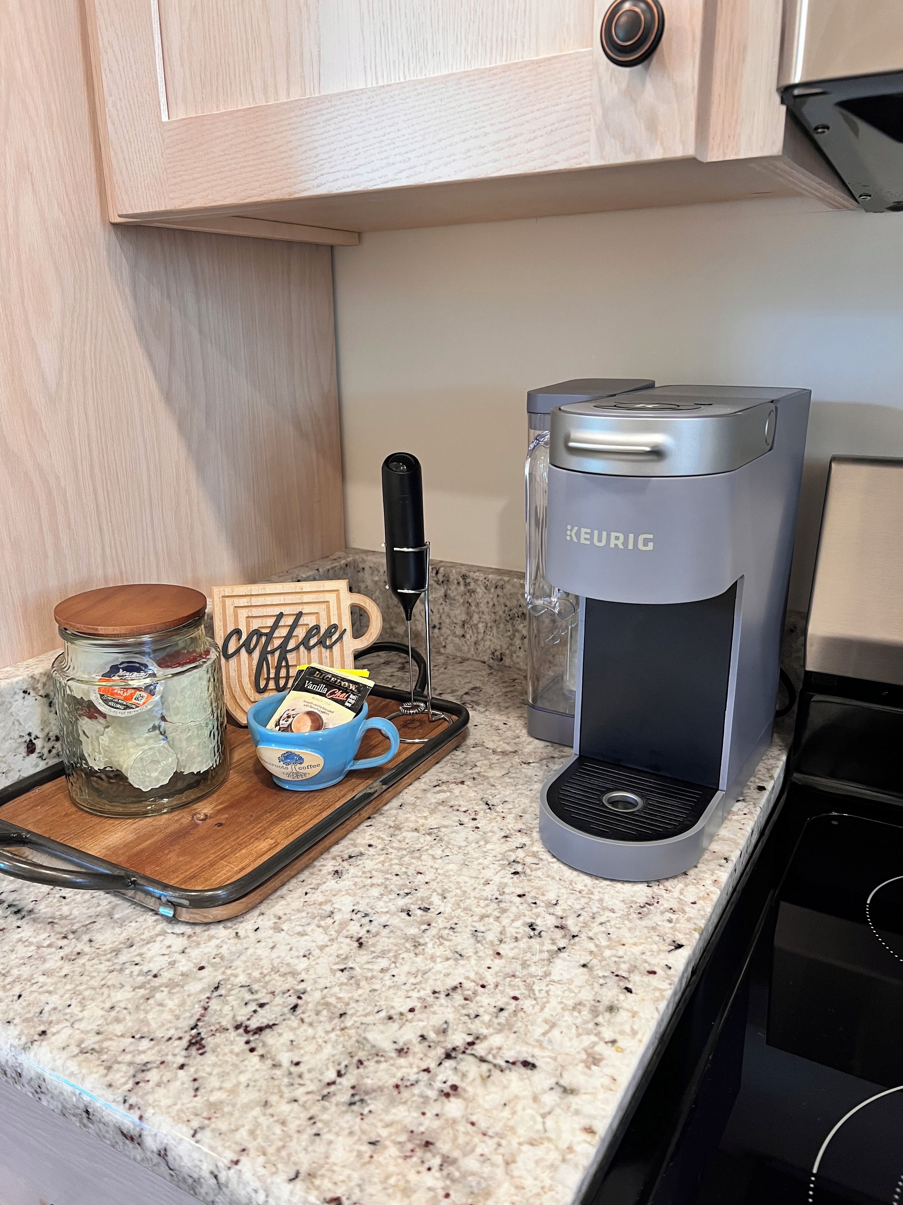 Eine Küchenarbeitsplatte mit einer Keurig-Kaffeemaschine, einem Kaffeiglas, einer Tasse und einem Holztablett.