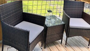 Un terrazzo in legno con sedie in vimini e un tavolo in vetro.