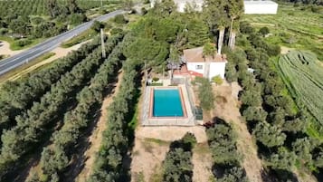 An aerial view of a property with a swimming pool, surrounded by dense trees and a road.