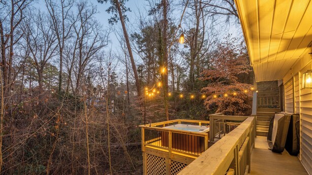 Eine Holzterrasse mit Whirlpool, umgeben von Bäumen und Lichterketten.