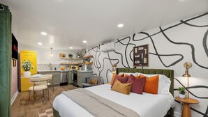 Ein modernes Hotelzimmer mit einem großen Bett, einer kleinen Küchenzeile, einem Essbereich und einem Badezimmer.