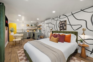 Ein modernes Hotelzimmer mit einem großen Bett, einer kleinen Küchenzeile und einem Essbereich.