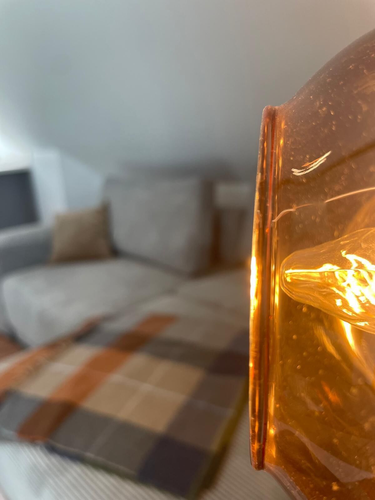 A close-up of a glass with a warm liquid, possibly a drink, in a modern living room with a sofa and a checkered rug.