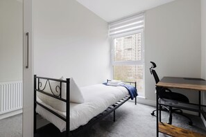 Een slaapkamer met een enkel bed, een bureau en een stoel.