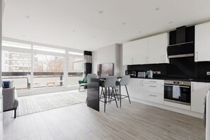 Een moderne keuken met witte kasten, een zwart aanrecht en een eethoek met een tafel en stoelen.