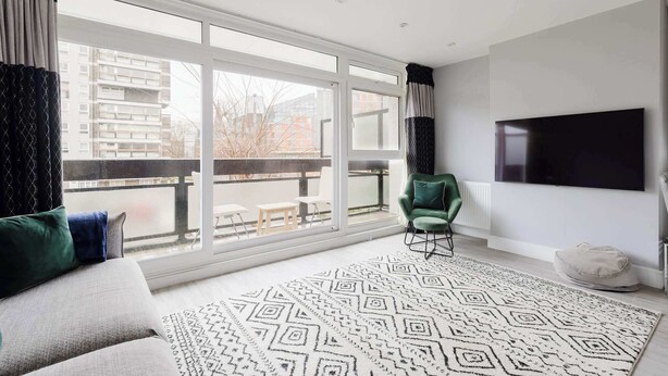 A modern living room with a large window, a flat-screen TV, a green armchair, and a patterned rug. - Contemporary 3BDR Retreat in South West London (Greater London)